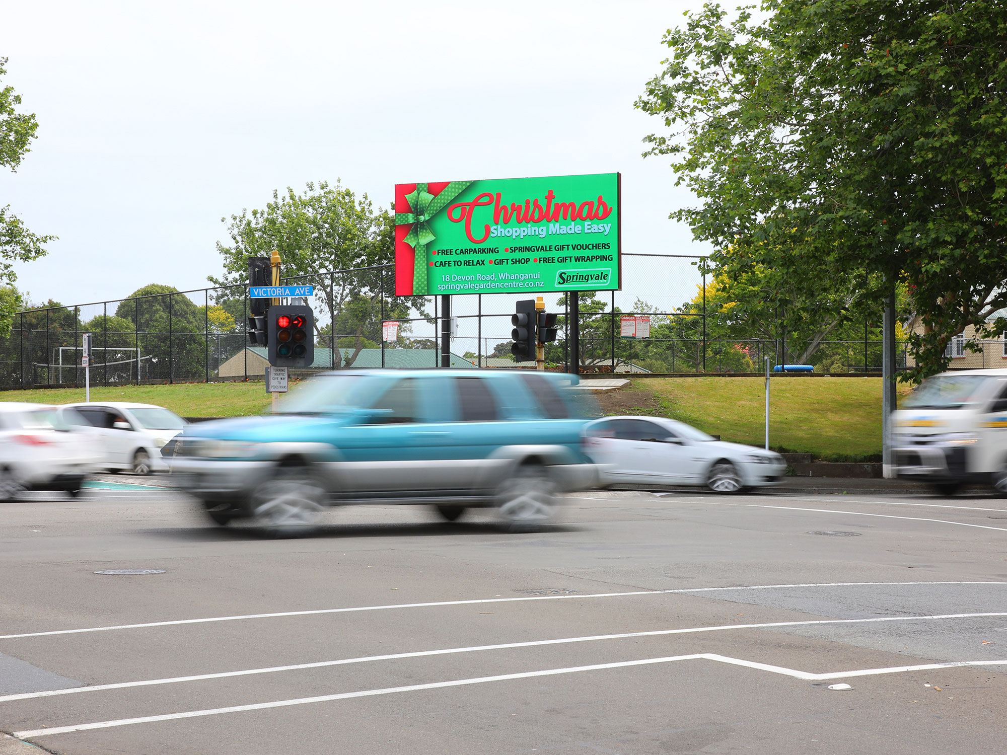 MAD's Whanganui Board on the corner of Dublin and Victoria Street. Car's wiz and wait and the traffic lights.